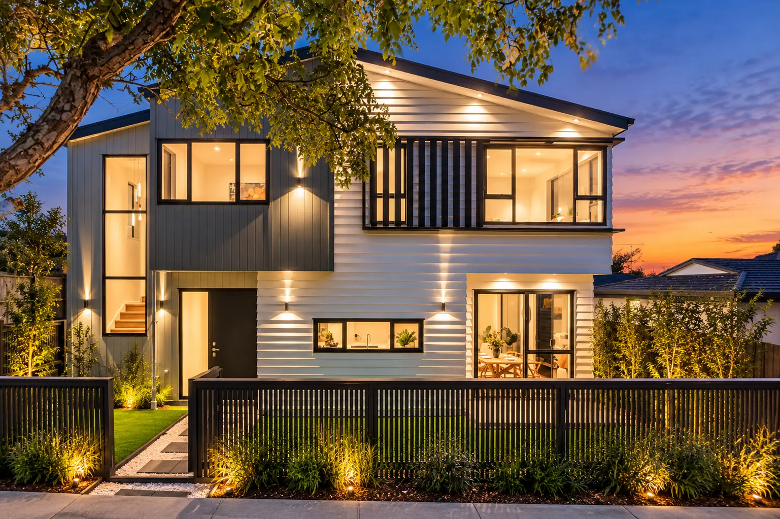 Street-front home with light cladding, dark detailing and landscaped boundary at dusk