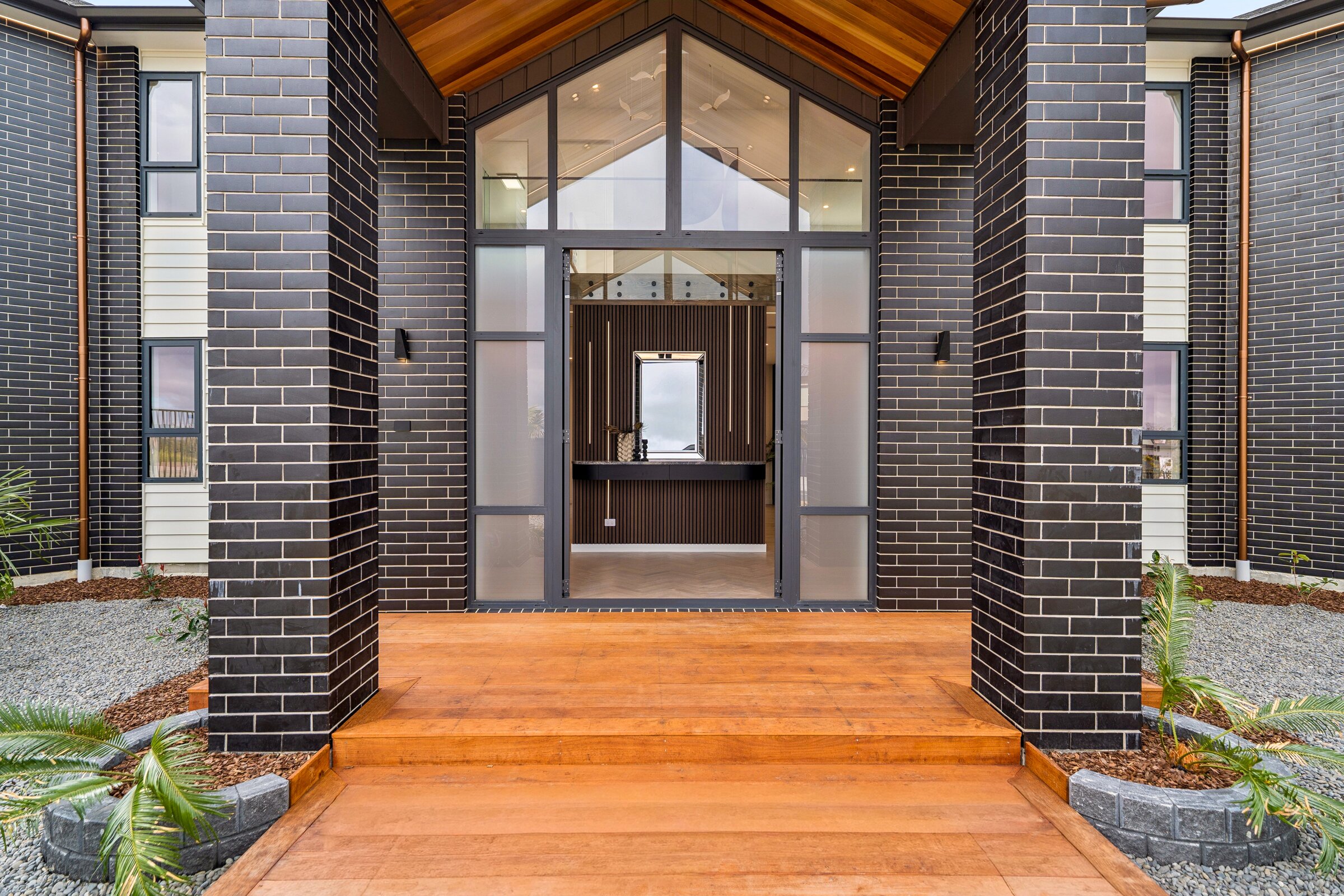 Central entry of 73 Kewa Road framed by dark brick, timber soffits and generous glazing